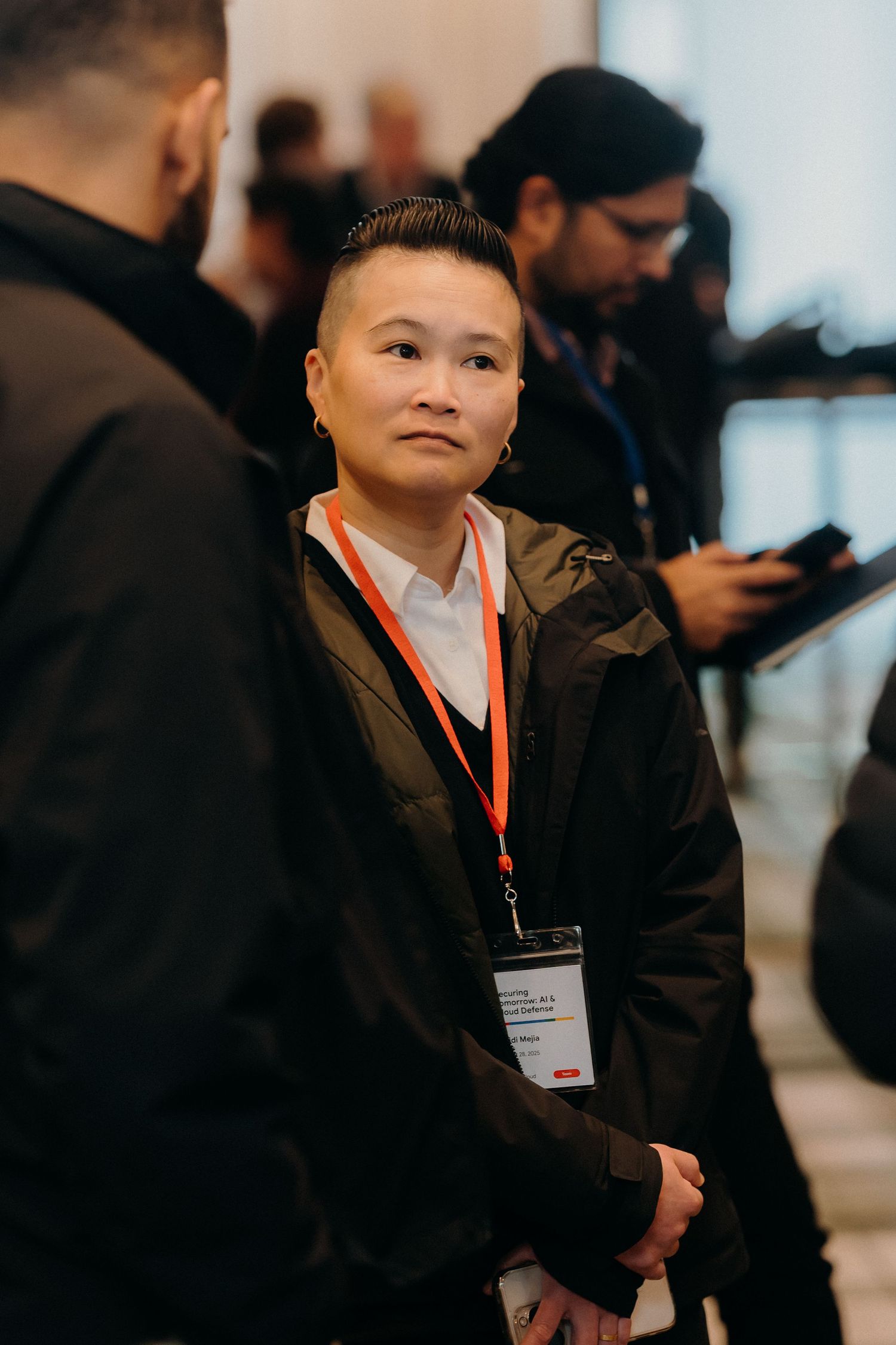 Young attendee wearing a lanyard and dark jacket looks up with curiosity during a professional event.