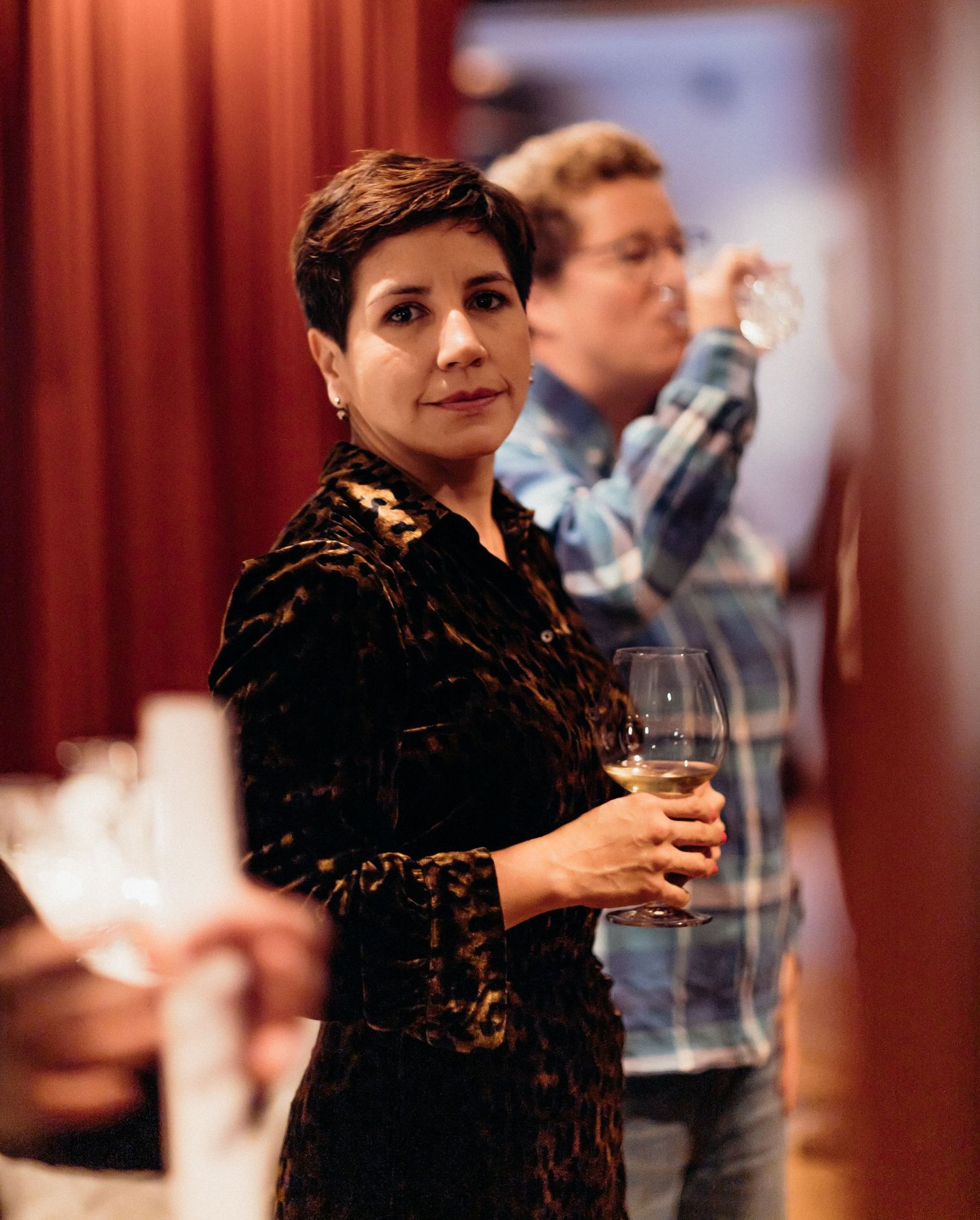 A person in a black lace top holds a wine glass while mingling at an indoor social event.