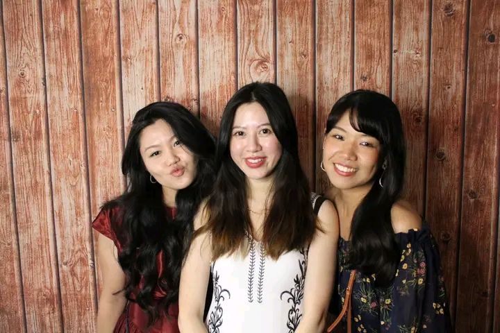 A group of women pose together in front of a rustic wooden wall background.
