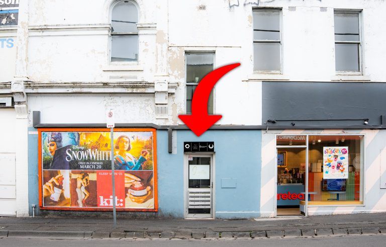 A panoramic view of a row of storefronts with windows and signs along a city street.