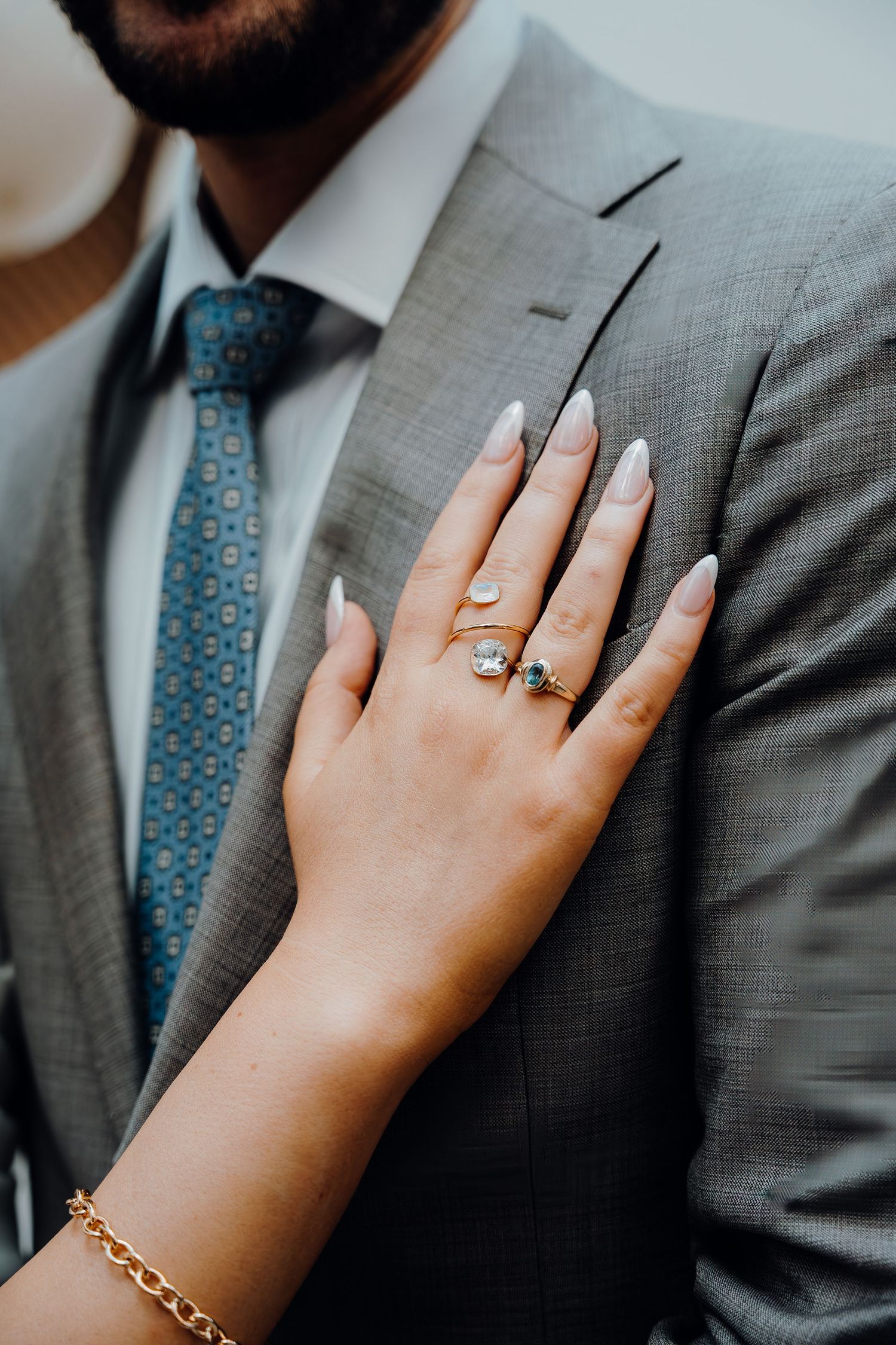 Close-up view showing bride placing hand on groom's suit with engagement ring and delicate gold bracelet.