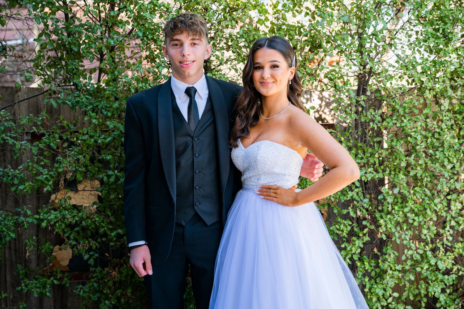 Bride and groom share romantic wedding photos in a lush garden setting with white floral backdrop.