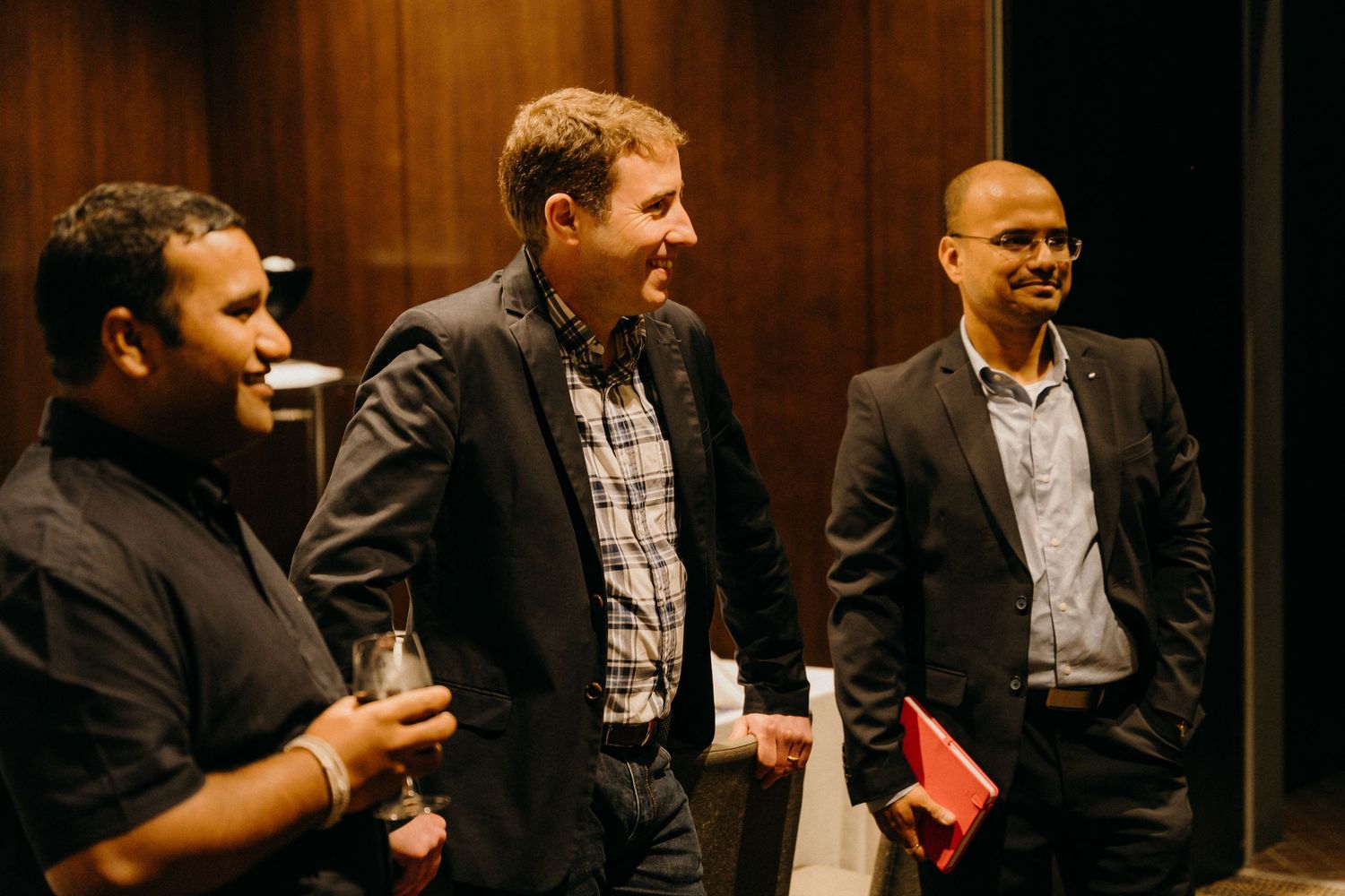 Three professional men smiling and networking at a corporate event, dressed in smart casual and business attire.