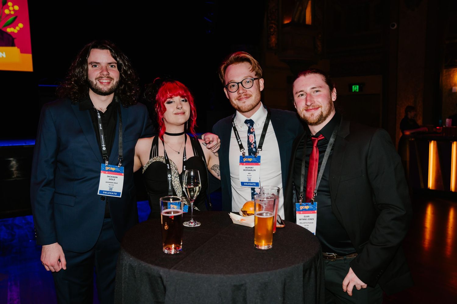 A group of four people standing around a small table with drinks at an evening networking event.