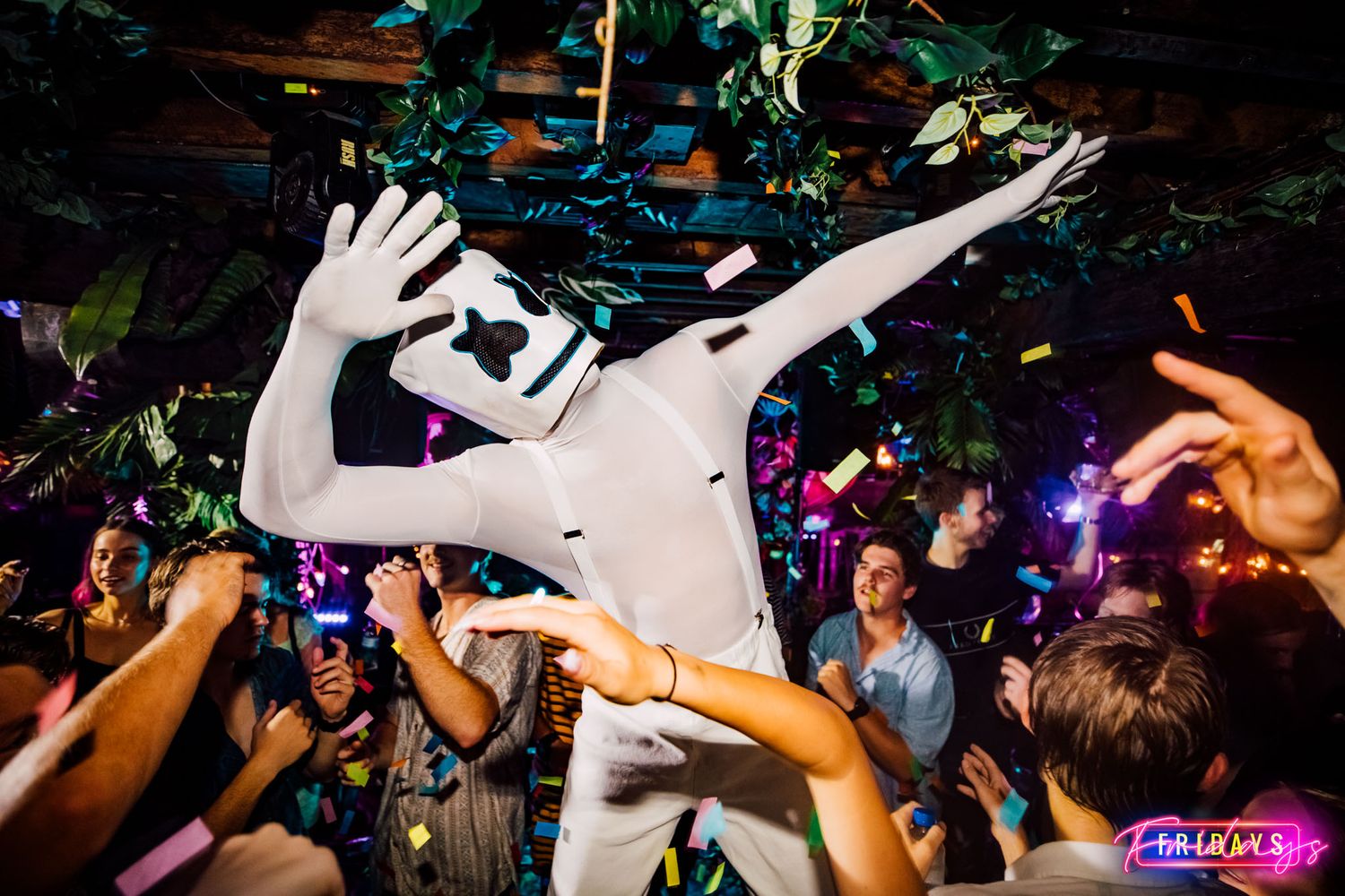Energetic crowd dancing at a nightclub with colorful lights and hands raised in celebration.
