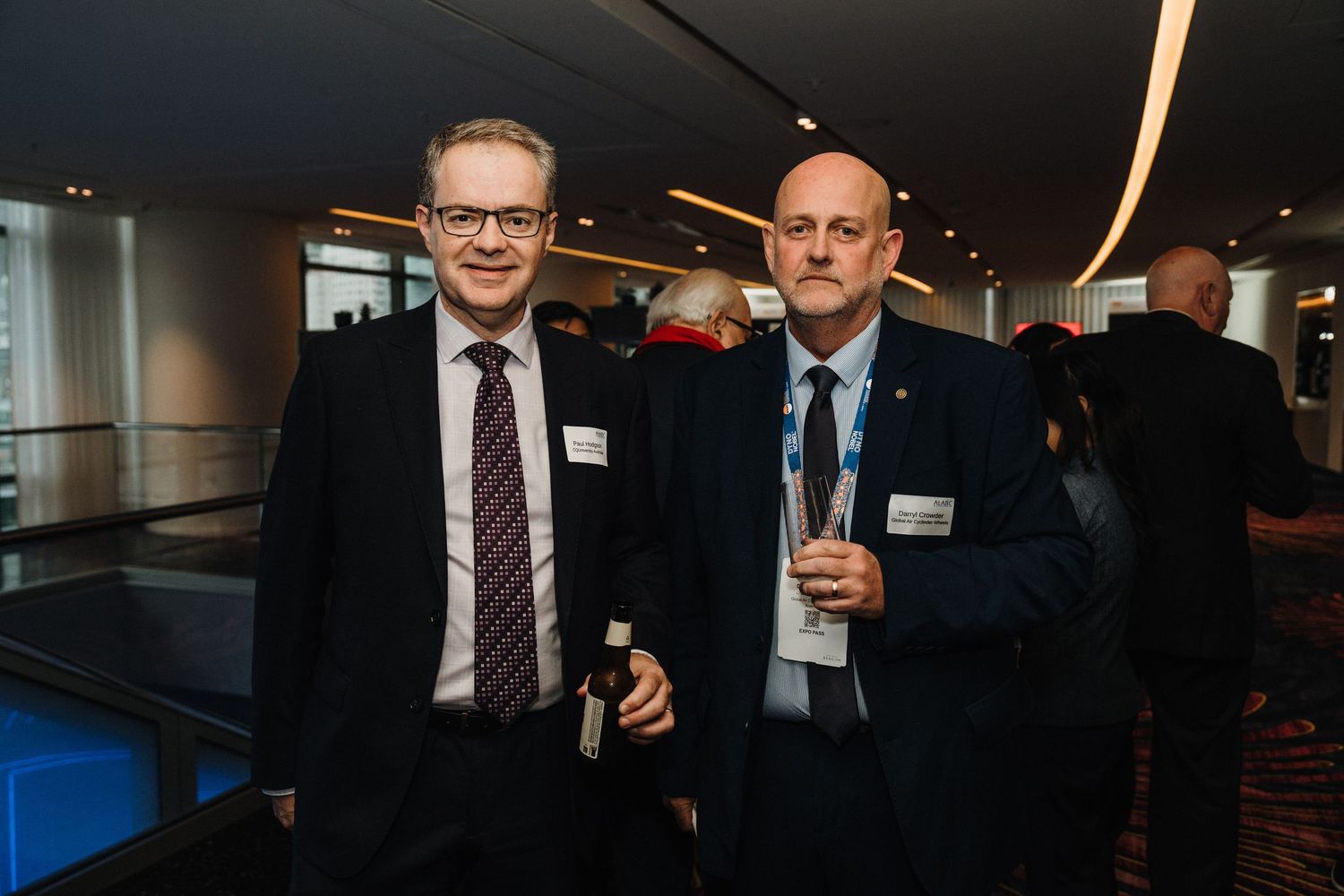 Two business professionals in suits stand together at an event with blue lighting in the background.