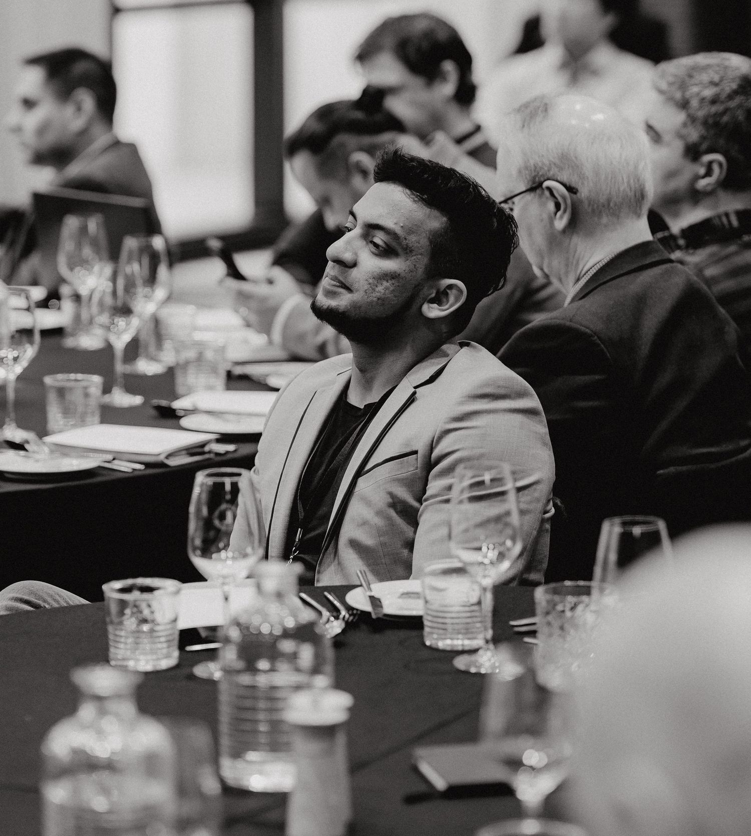 People sitting at a business conference table with drinks and papers, captured in black and white.
