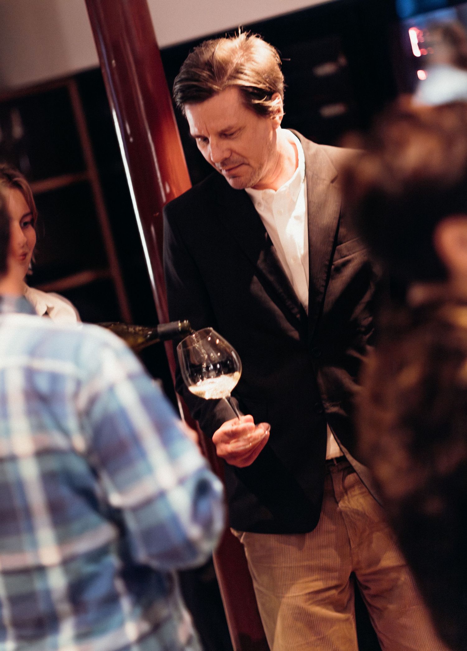 Person in formal attire examining a glass of wine in a dimly lit restaurant setting.