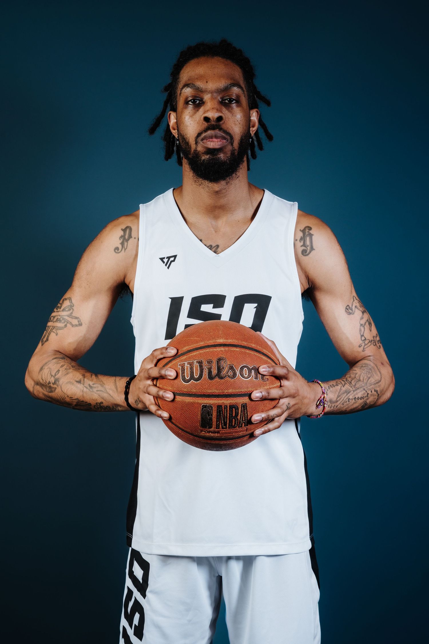 Basketball player in white jersey holds official NBA basketball against dark blue studio background.