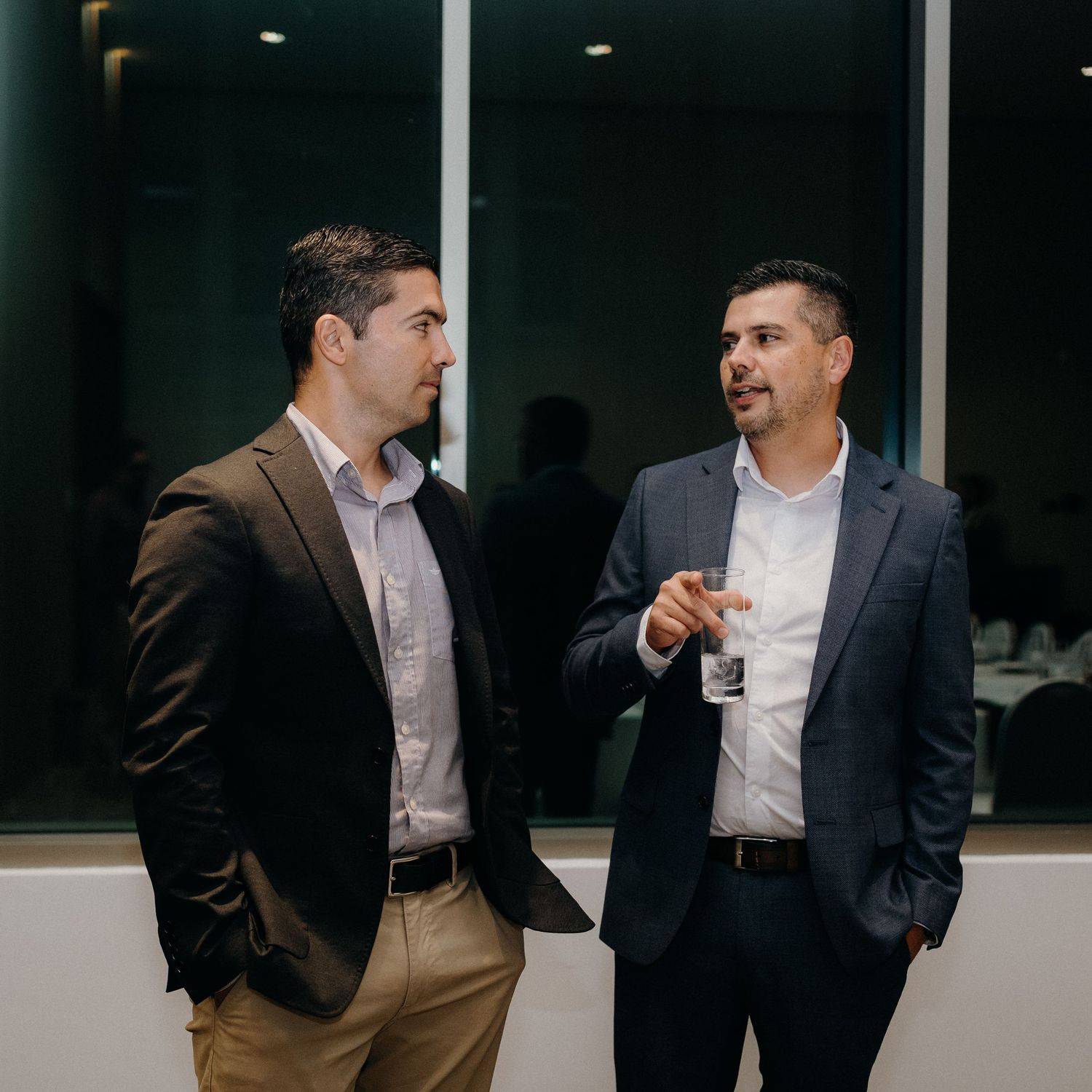 Two businessmen in suits having an animated conversation in a modern office hallway.