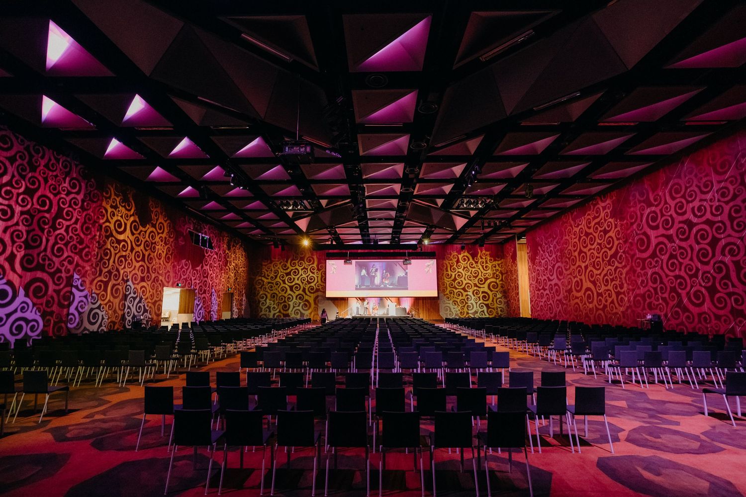 Modern nightclub interior with pink and purple LED lighting illuminating geometric ceiling patterns and lounge seating areas.