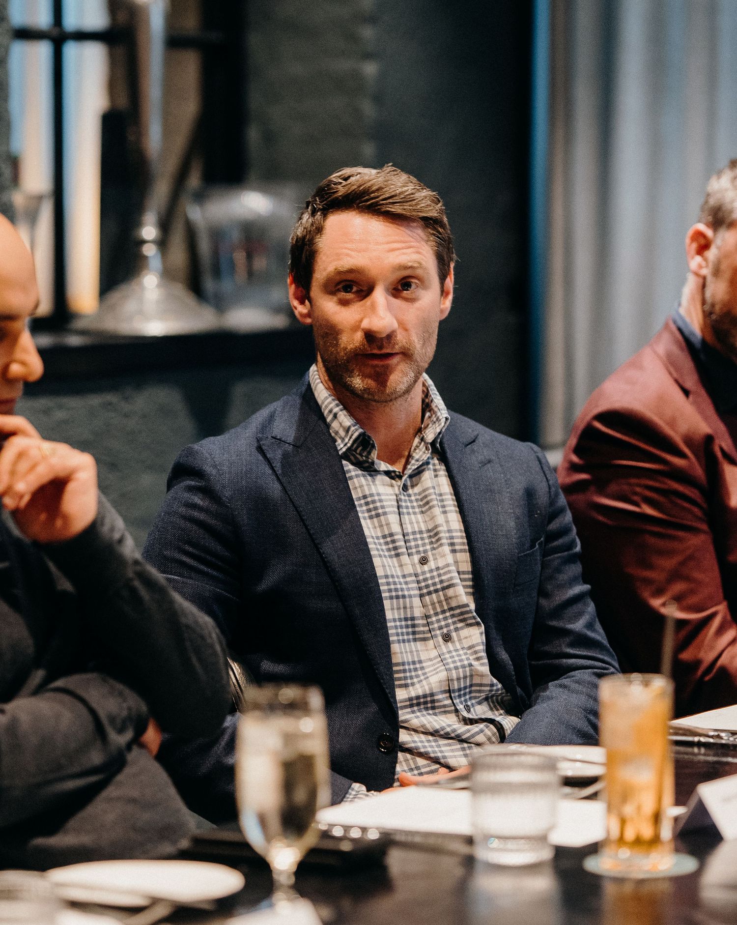 A person in a navy blazer and checkered shirt sits at a restaurant table during a meal.