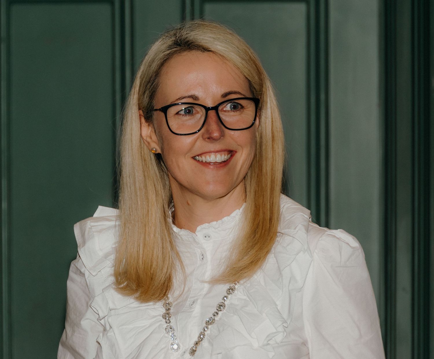 A person wearing glasses and a white blouse poses against a green wall in a series of three similar photos.