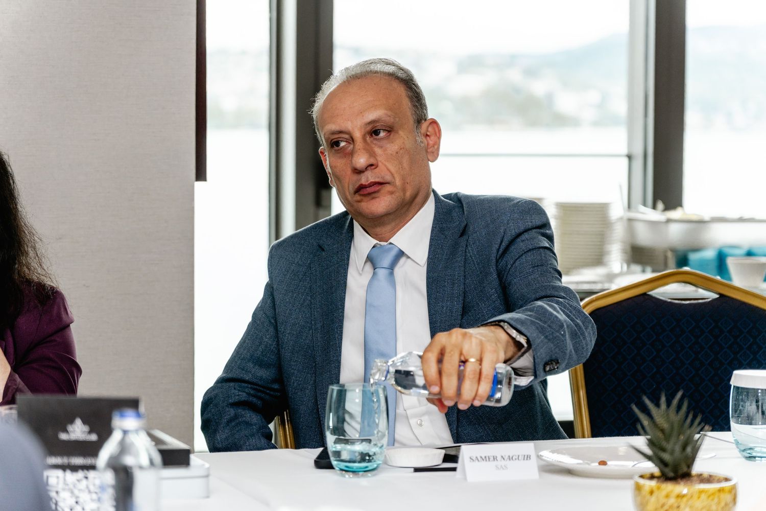 Professional man in blue suit seated at conference table during business meeting in modern venue.