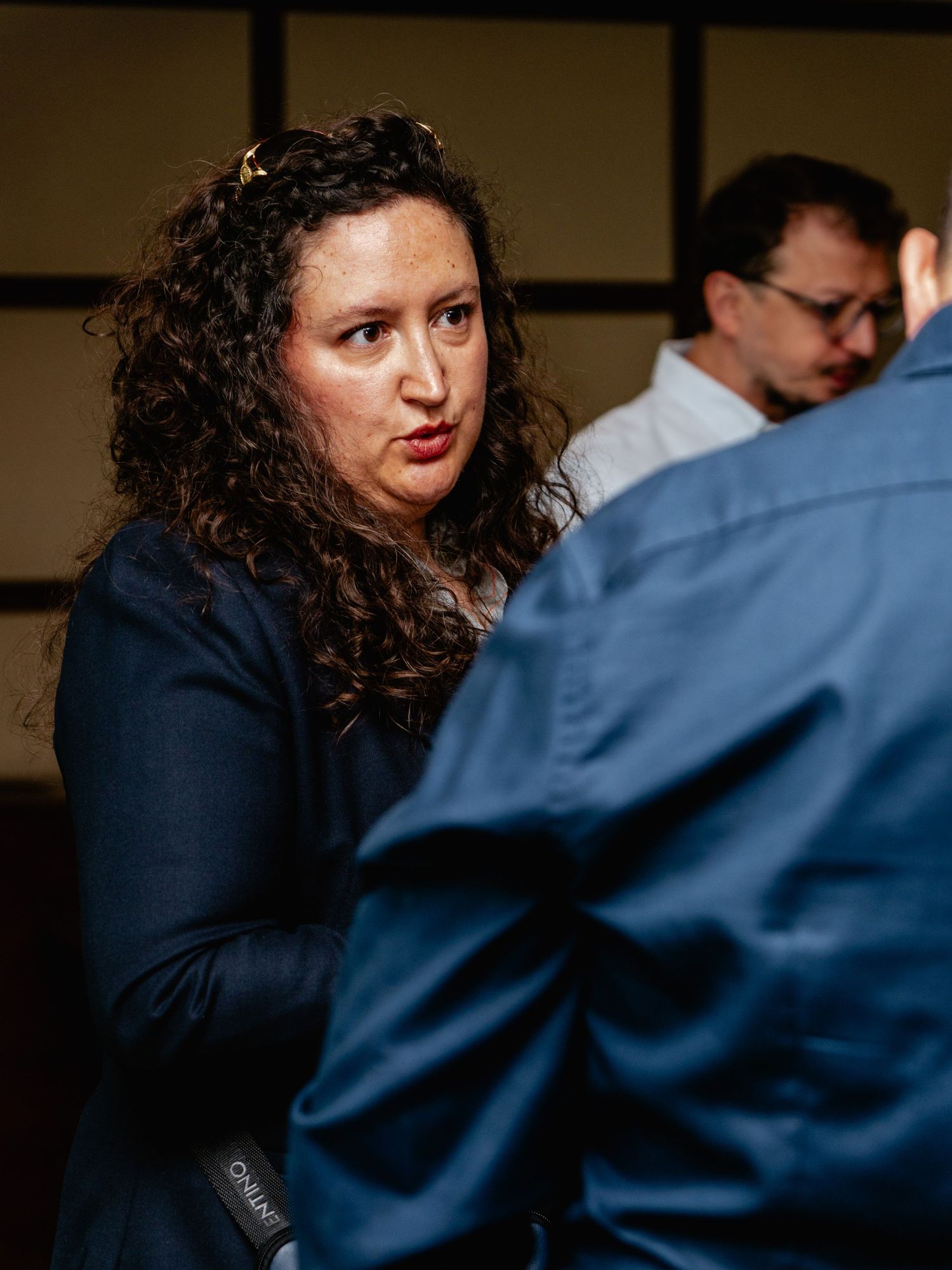 Woman with curly hair in blue blazer engaged in conversation at an indoor networking event.