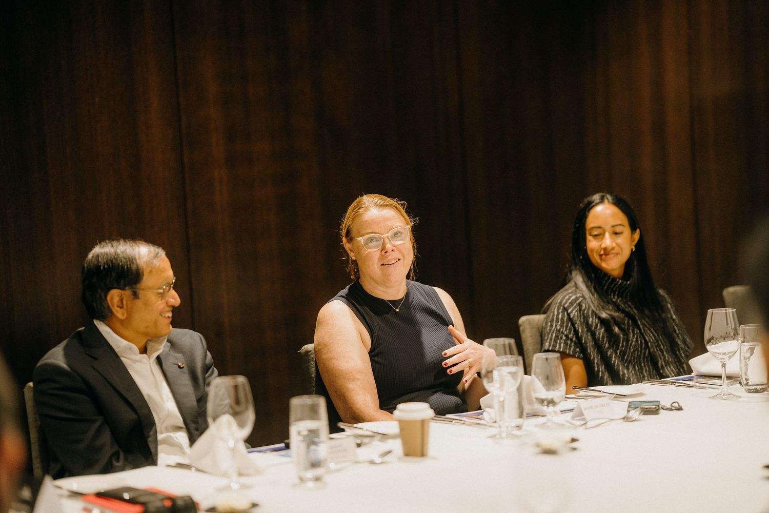 Three professionals seated at a formal dinner table, smiling and engaged in conversation in an elegant venue.