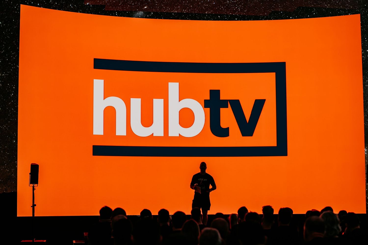 Orange and black NDTV news channel logo and branding displayed on a dark background.