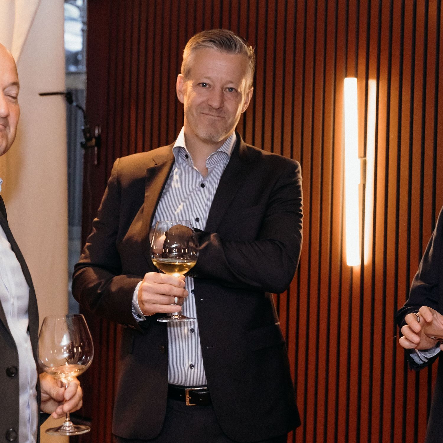 Business professionals in formal attire gather at an event while holding wine glasses for a networking reception.