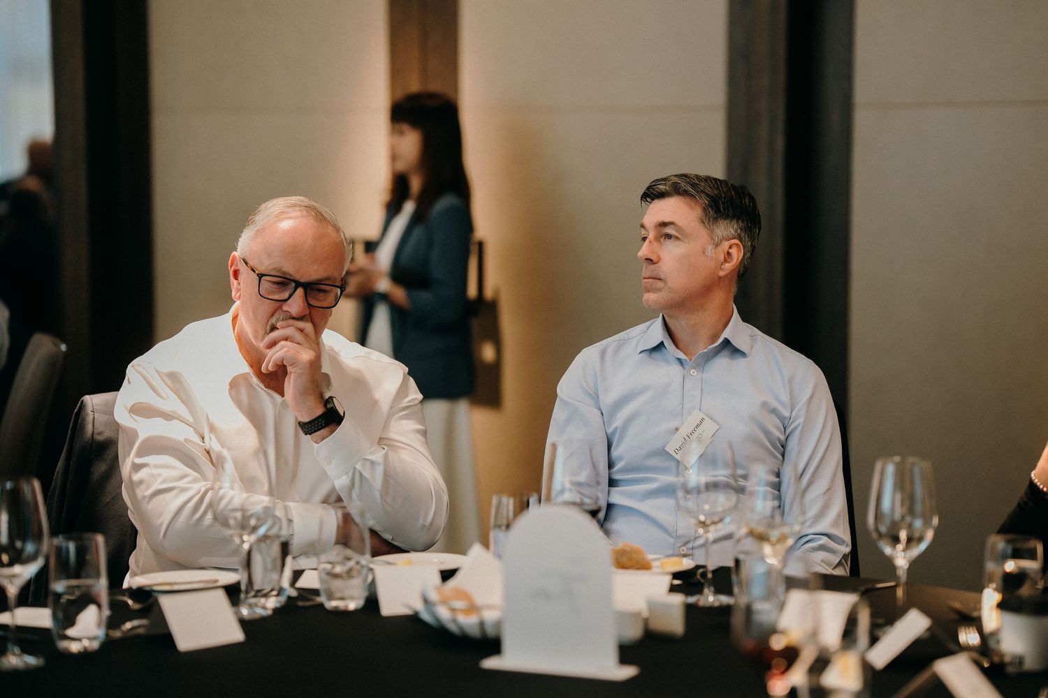 Business professionals sitting at a conference table during a meeting with wine glasses and documents.