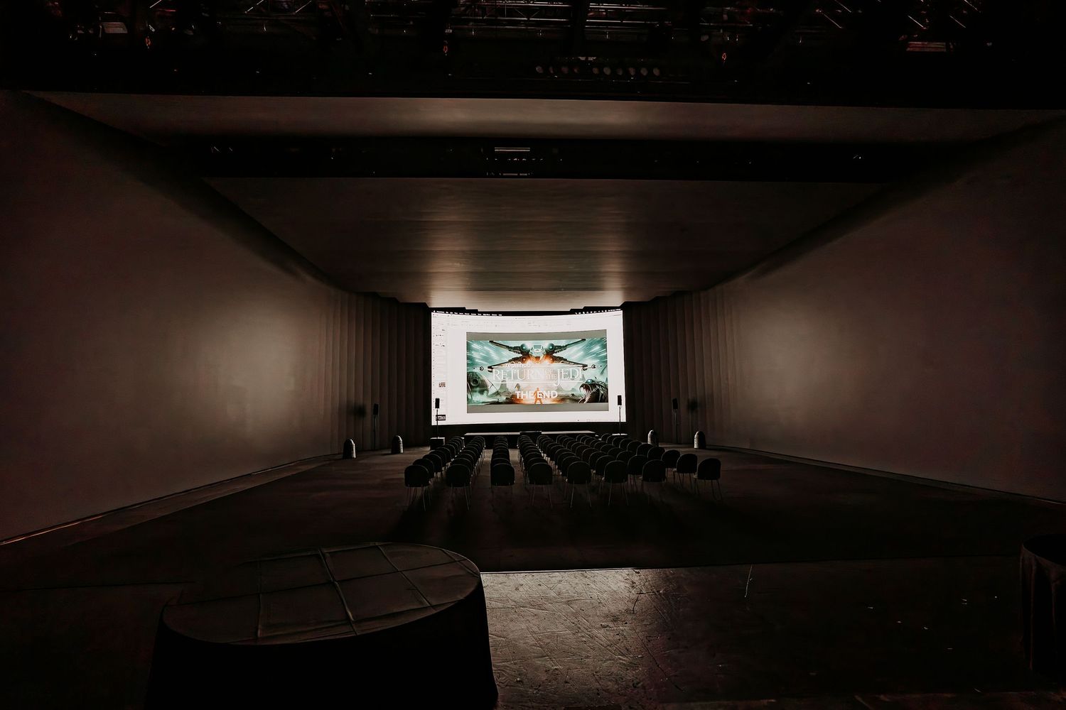 A dark home theater room with stadium seating and a large projection screen displaying content at the front.