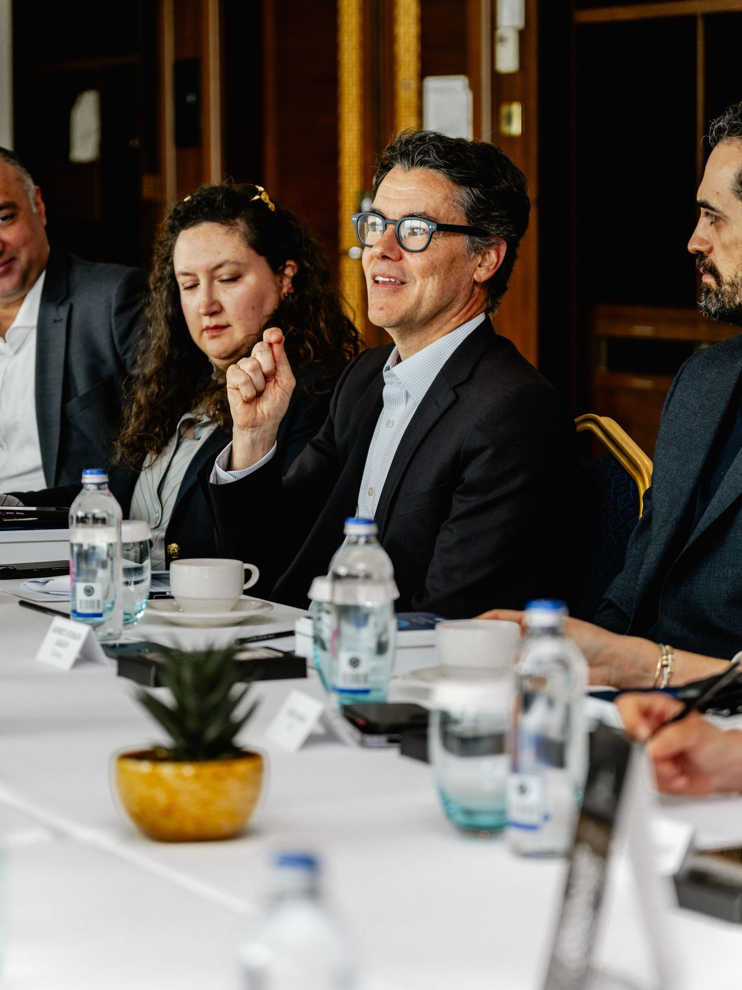 Business professionals seated at a conference table during a formal meeting, with water bottles and documents visible.
