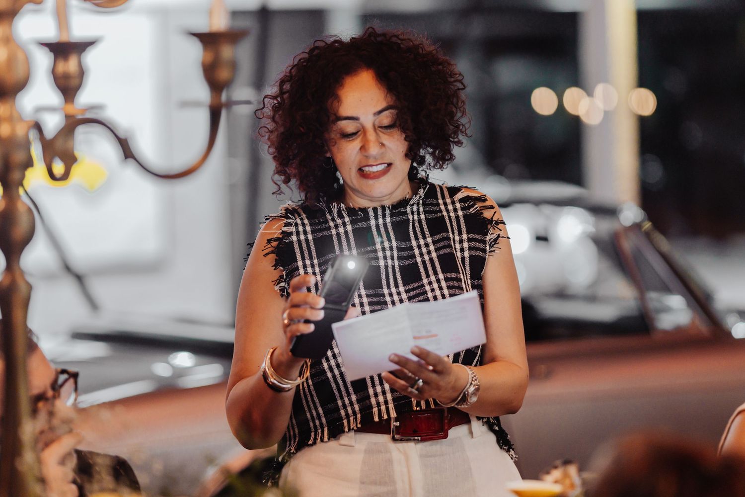 Professional in plaid blouse laughs while reading text message on smartphone in evening office setting.