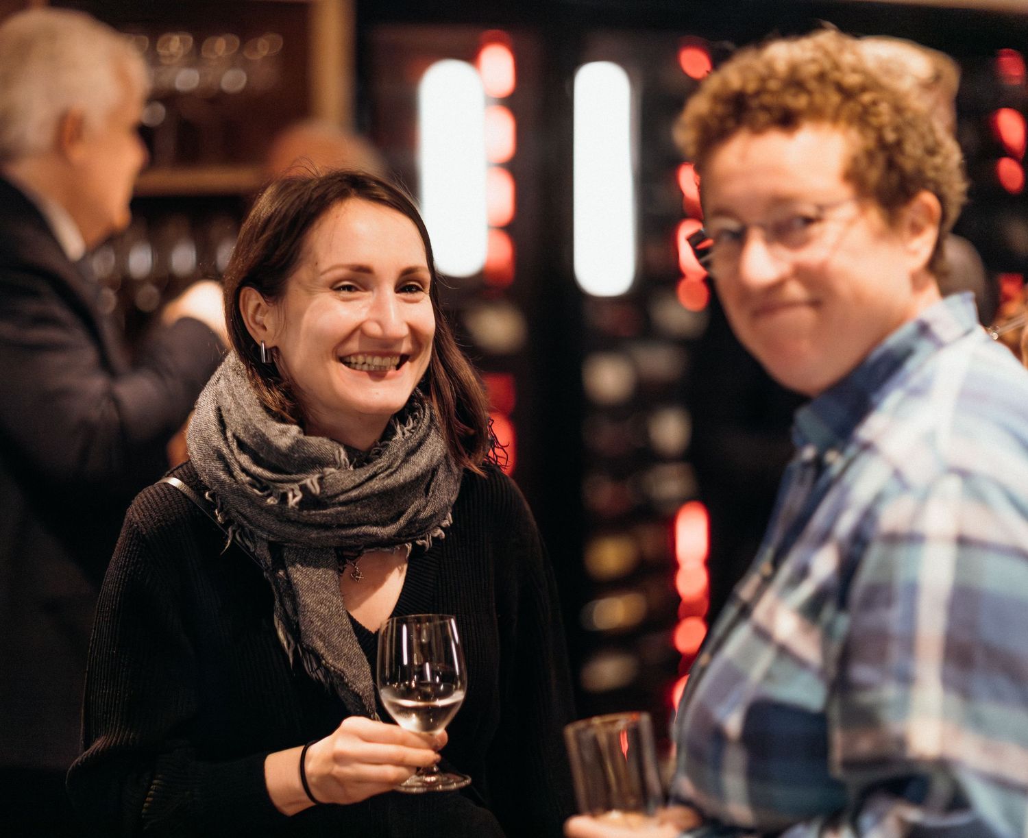 People enjoying wine and conversation at a dimly lit bar with red lighting in the background.