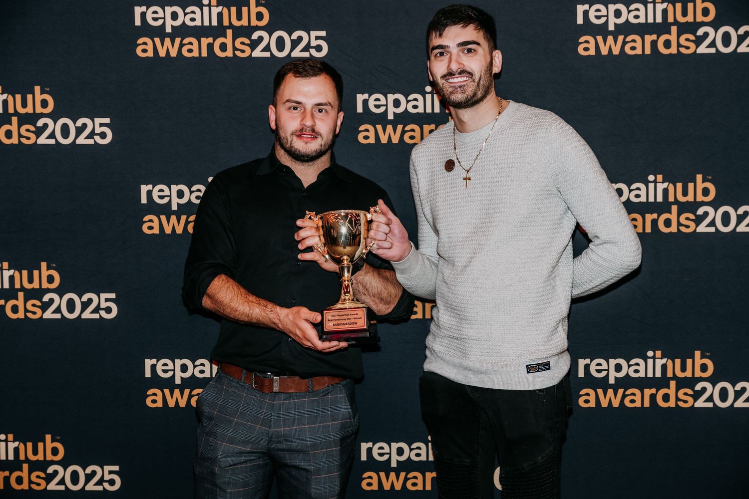 Event attendees pose for photos against a branded RepairHub Awards 2025 backdrop at a professional ceremony.