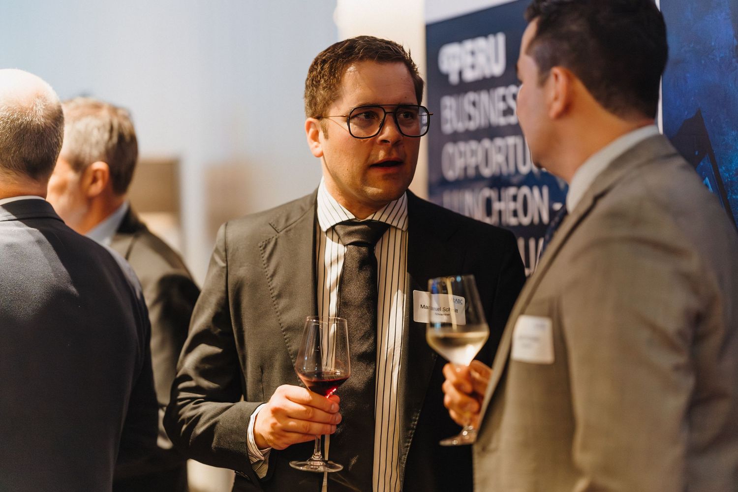 Business professionals network and socialize at a corporate event while holding drinks and engaging in conversation.