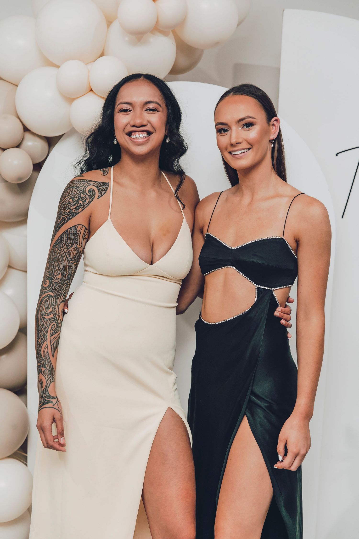 Group of women in black and cream colored swimsuits posing together against white balloon backdrop.