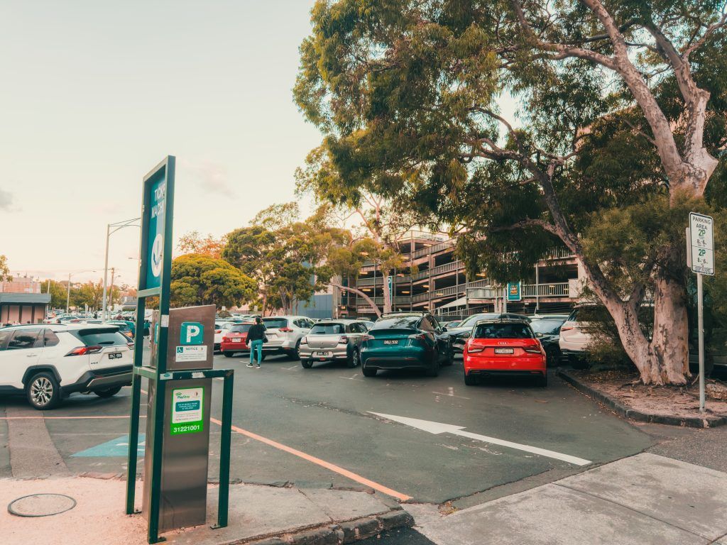 A panoramic view of a suburban parking lot with green trees and parked cars on a sunny day.