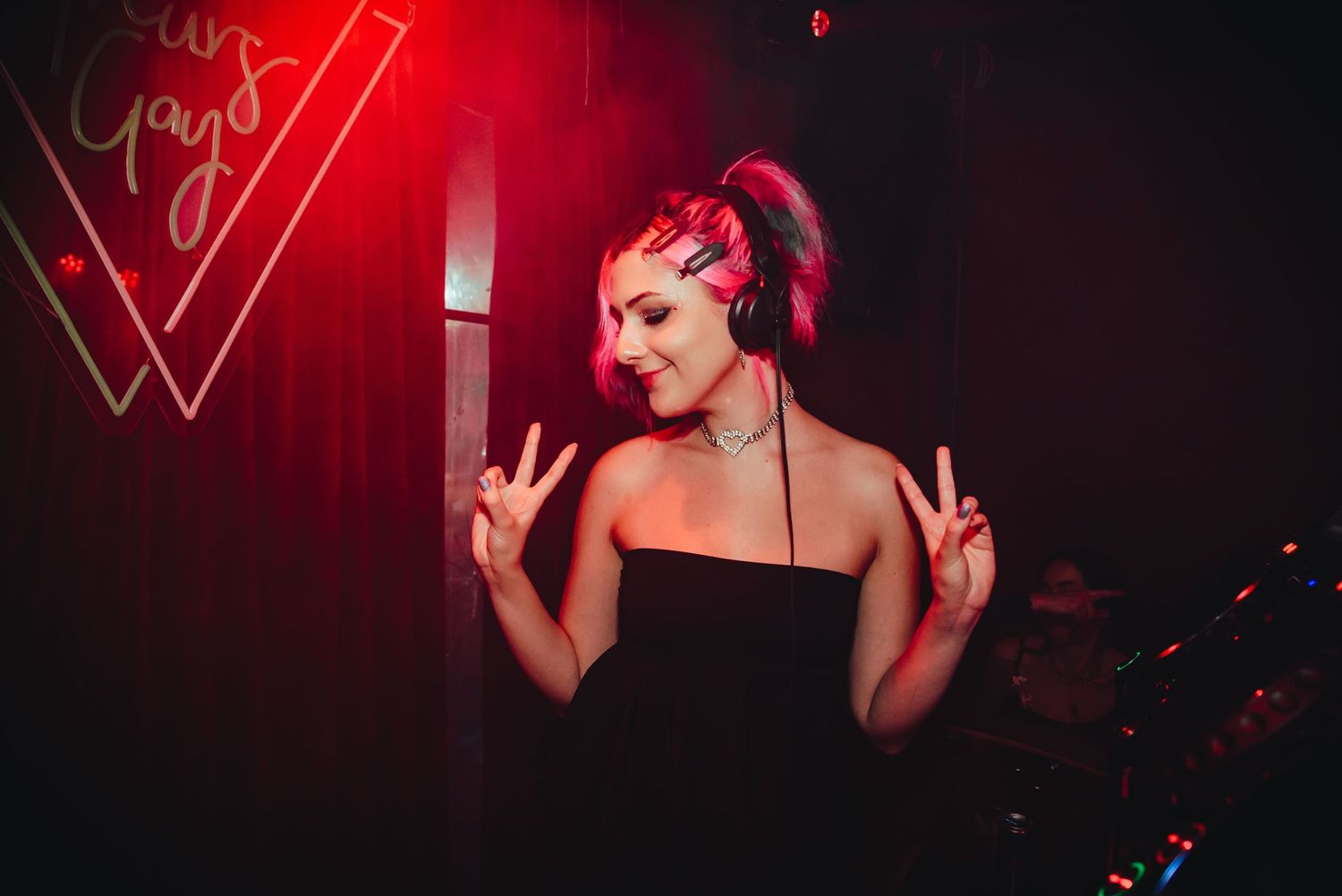 DJ performs at a nightclub with red lighting while gesturing to the crowd during an energetic set.