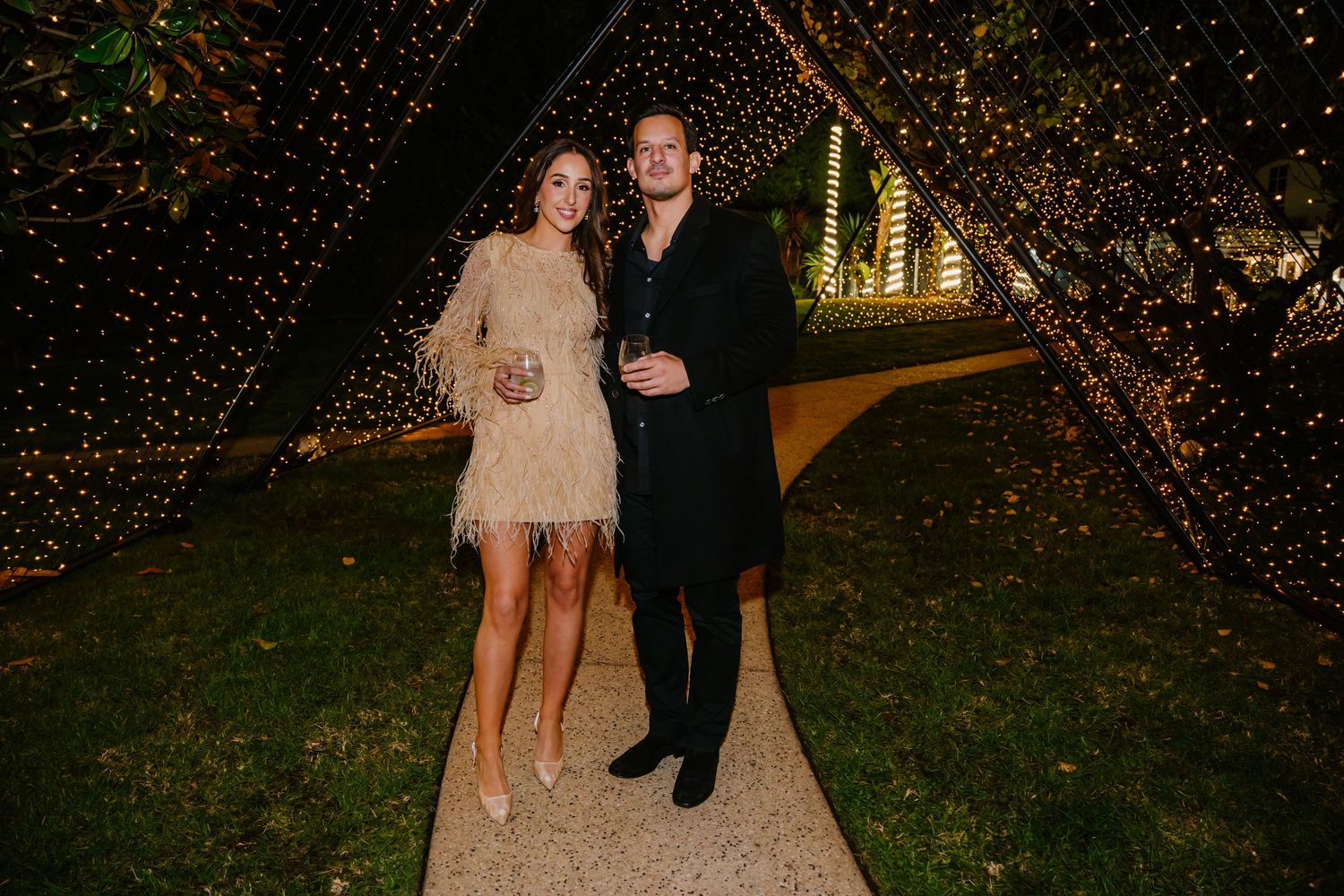 Wedding couple poses in front of glowing trees decorated with twinkling lights at an outdoor evening celebration.