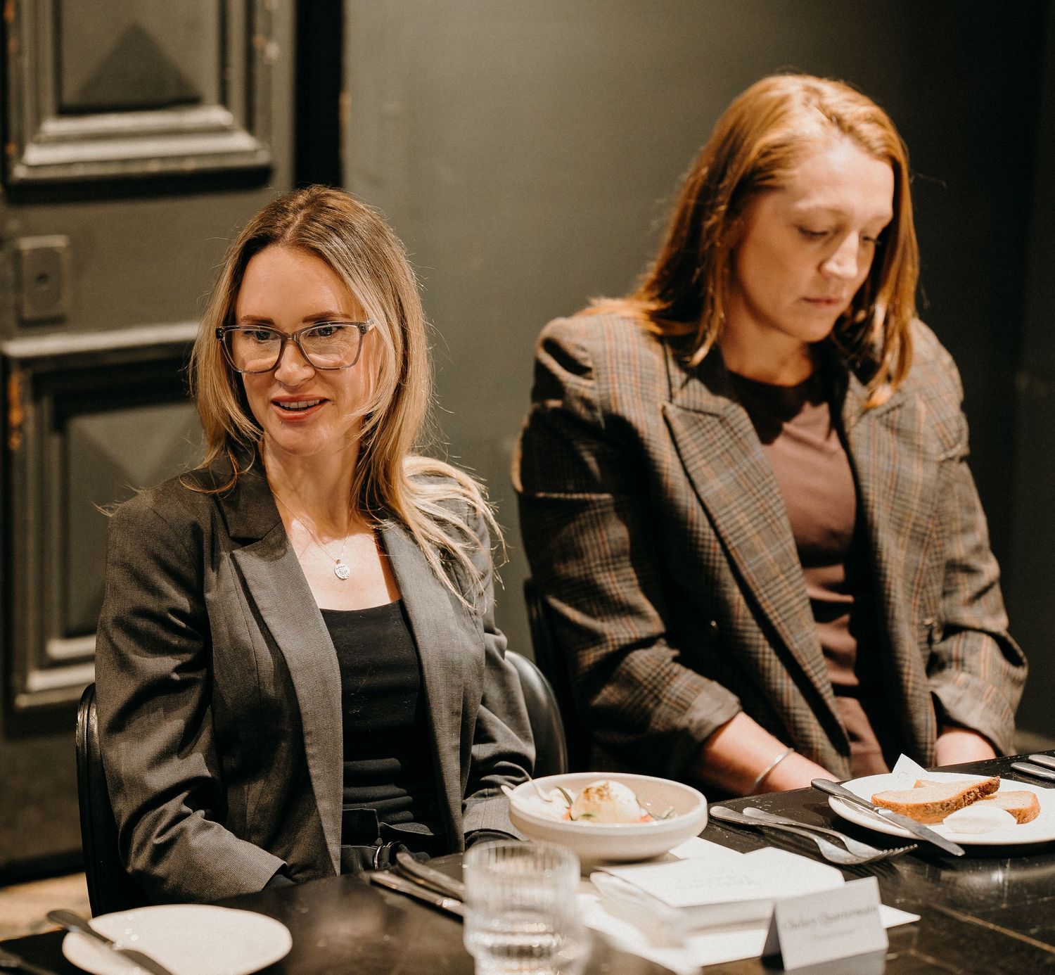 Professional wearing a gray blazer sits at desk writing notes in a modern office setting.