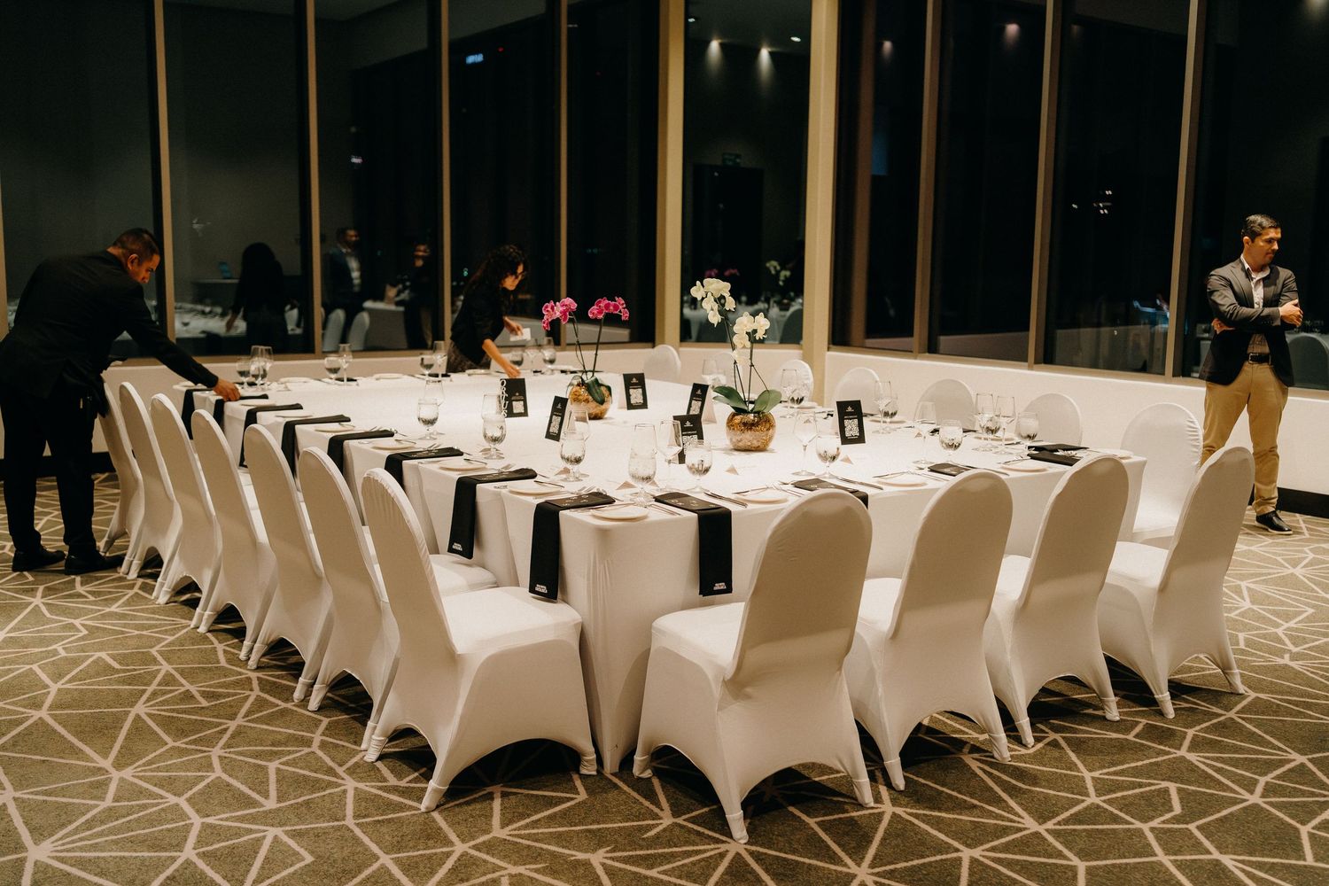 White spandex chair covers and elegant table settings create a sophisticated banquet hall atmosphere for an event.