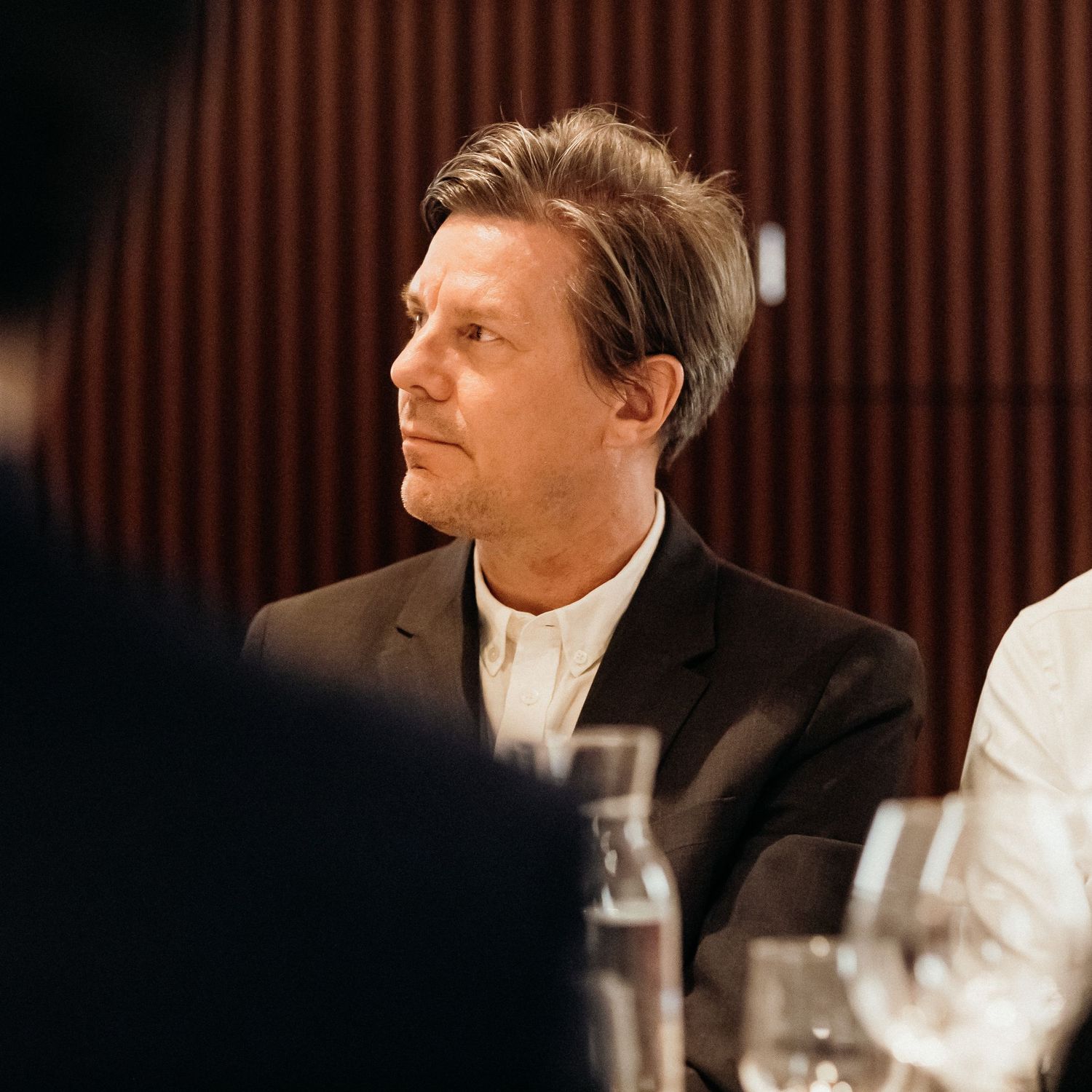 A person in a dark suit looking thoughtfully to the side during what appears to be a formal dining event.