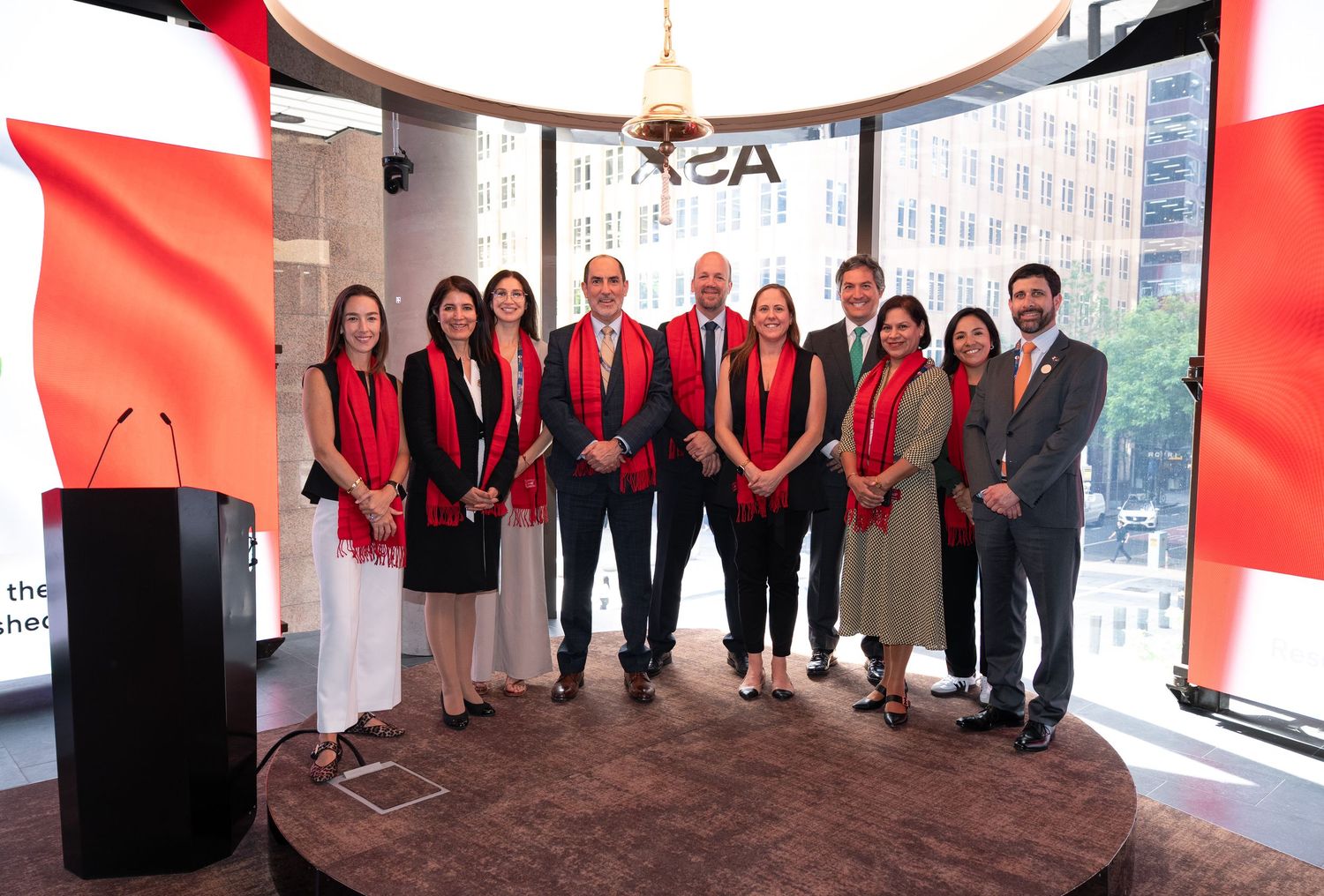 A group of people wearing red and black business attire stand in a line against a bright office window background.