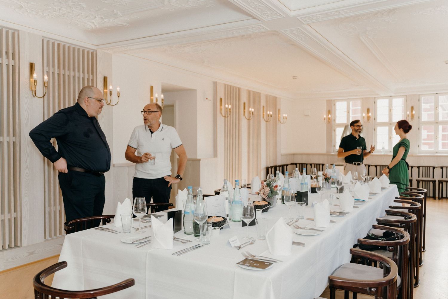 Elegant banquet hall setup with long white-clothed table, guests and staff preparing for a formal dining event.