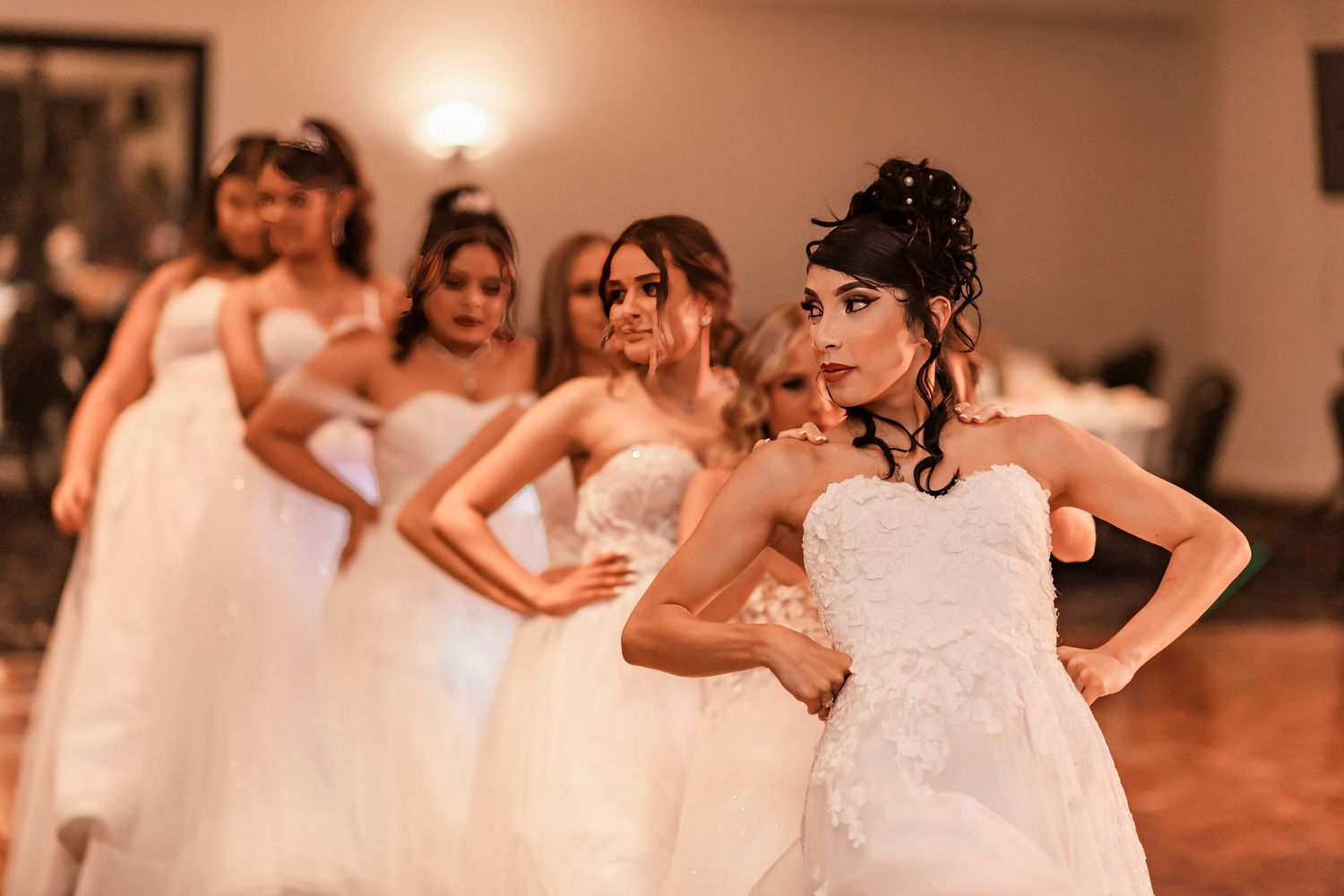 Group of people in white dresses dancing together during a celebration in a warm-lit interior space.