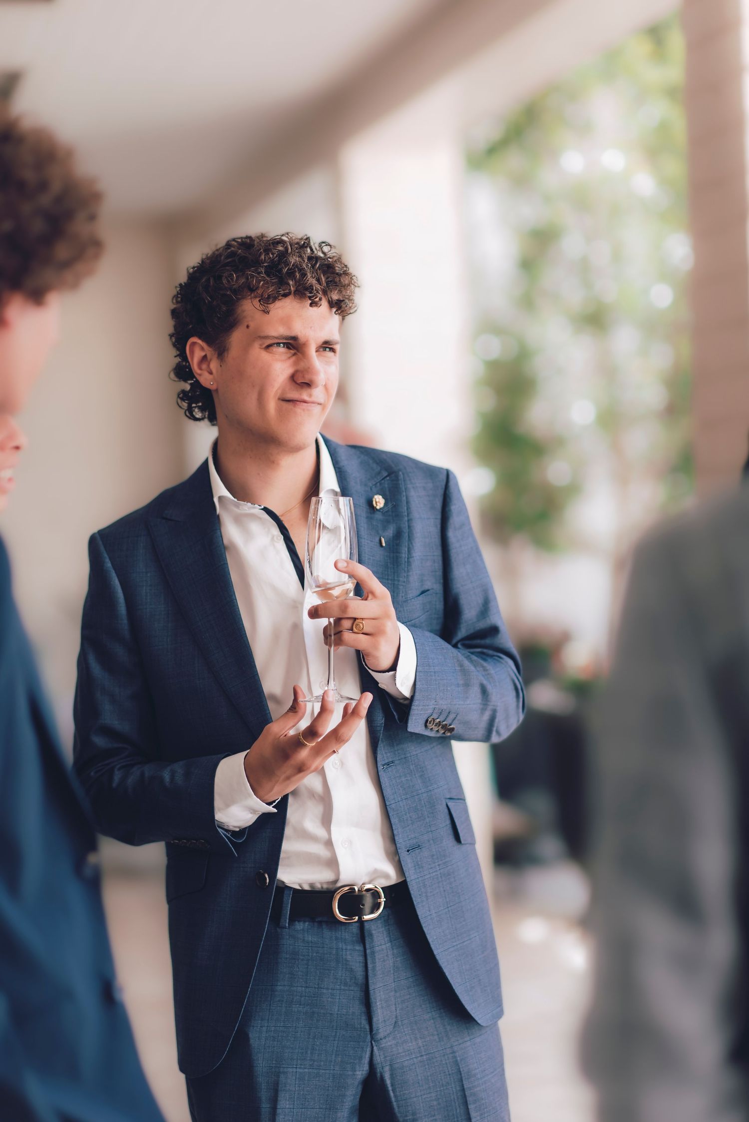 Person wearing a navy suit jacket and white shirt poses while holding a mobile phone.