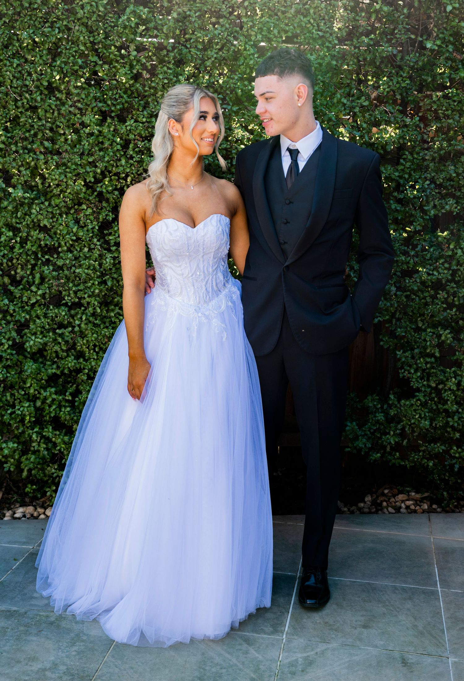 A couple in wedding attire poses against a lush green hedge background in various candid moments during their photo session.