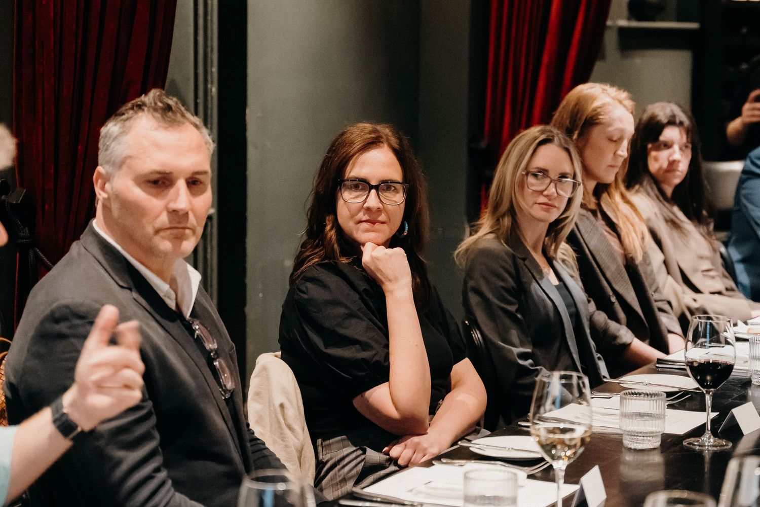 Business professionals sit at a long conference table during a meeting in a dimly lit room.