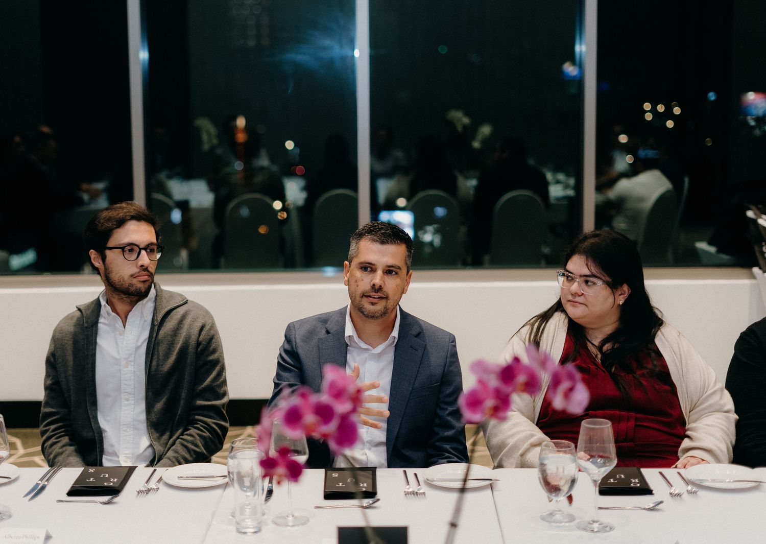 Business professionals seated at a long table during a formal dining event in a dimly lit room.