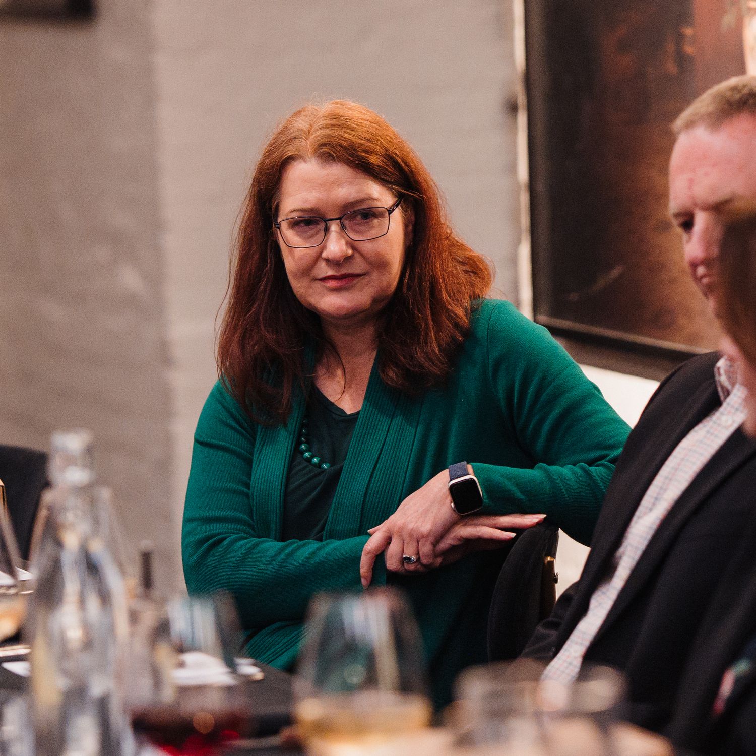 A person in a green sweater sits at a table during what appears to be a business meeting or dining event.