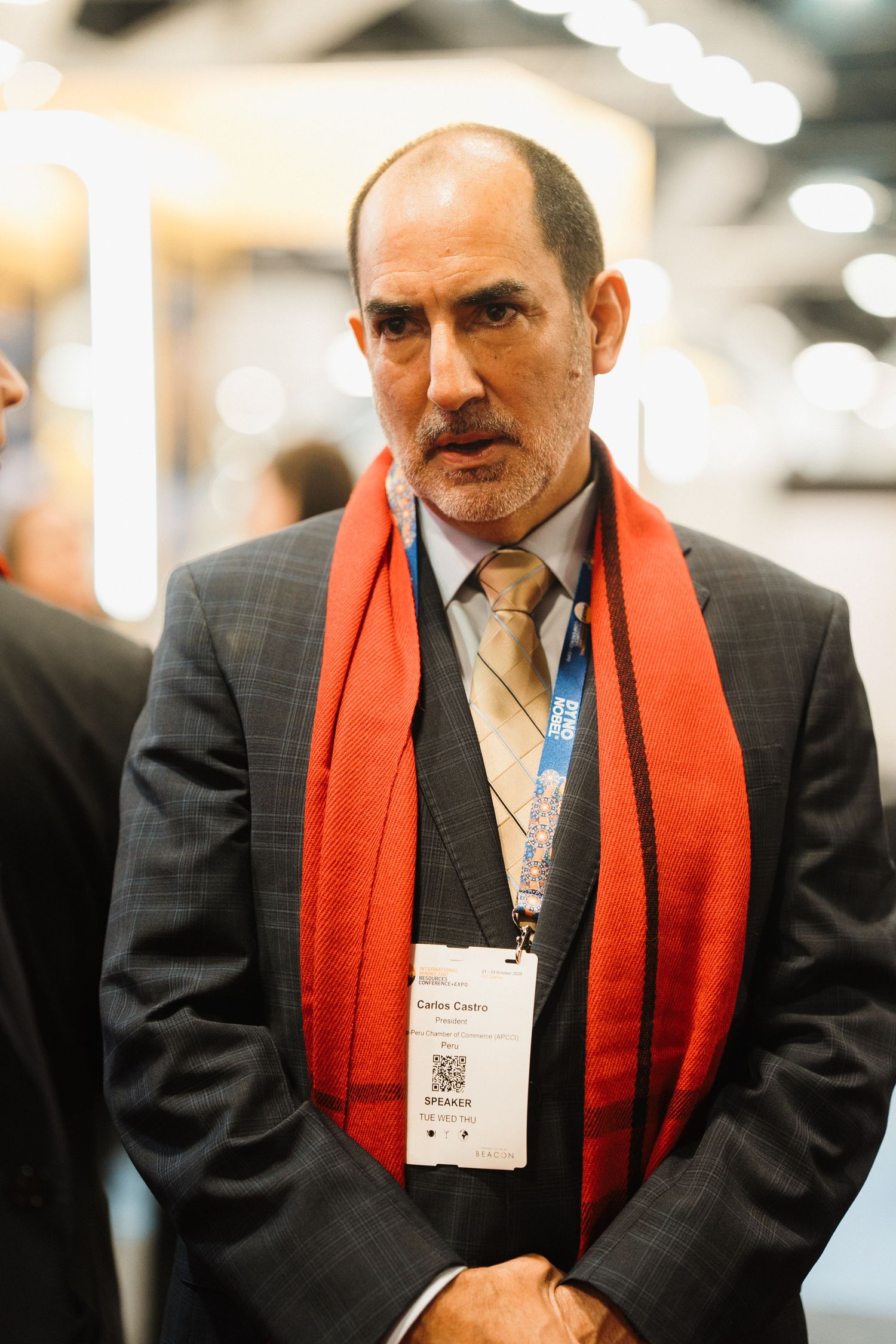 A person wearing a dark suit and bright orange scarf at a professional event with a name badge.