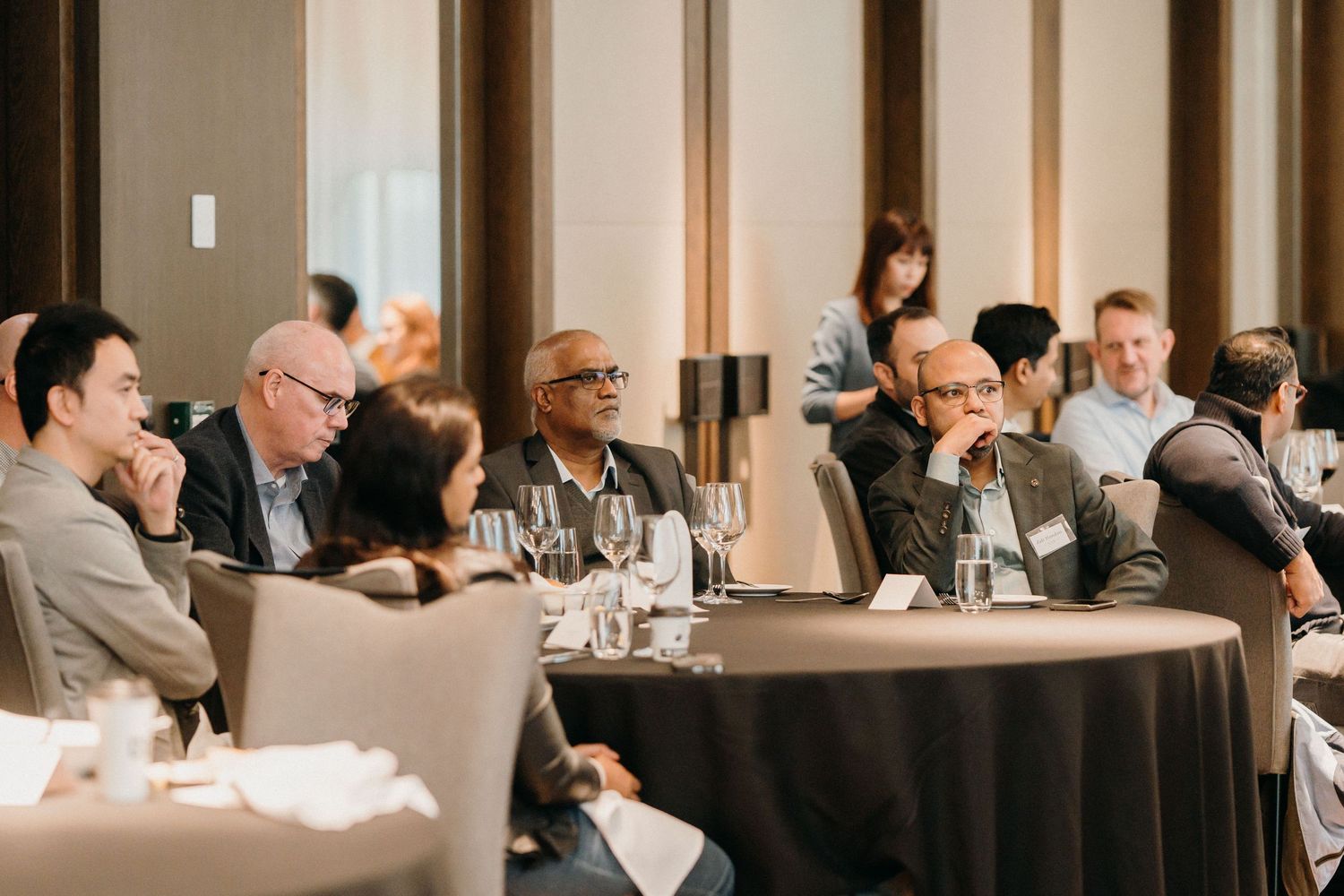 Business professionals sit at round tables during a corporate conference or meeting in an elegant venue.