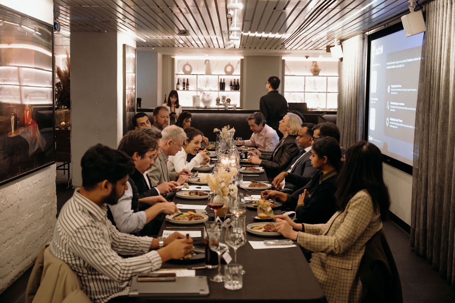 Business professionals attend a corporate meeting in a modern conference room with presentation screens.