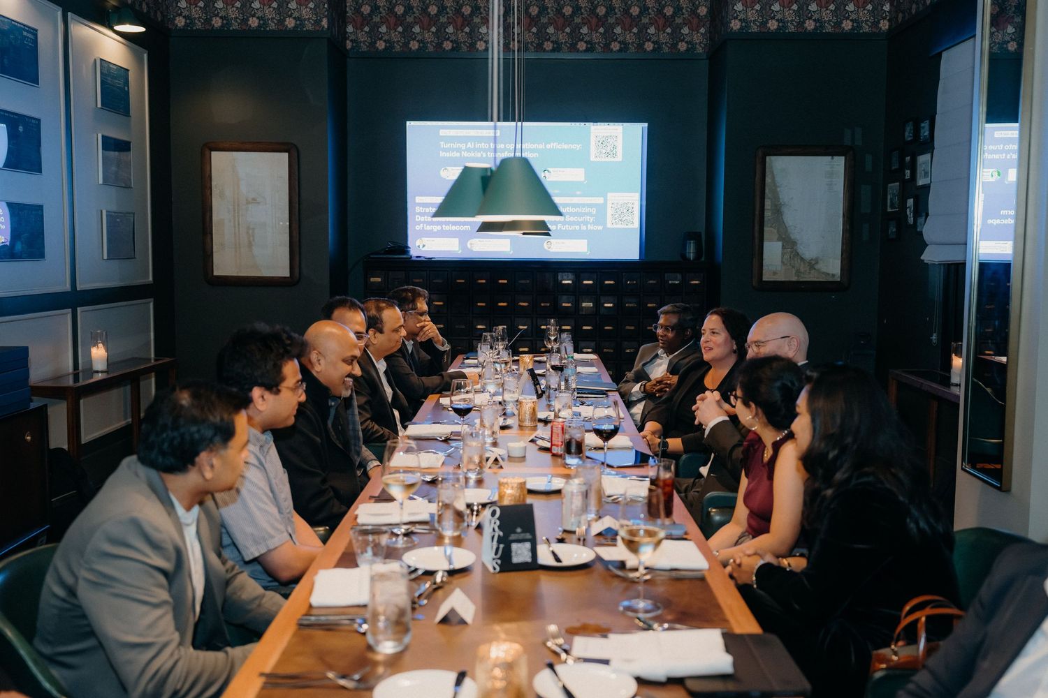 Business professionals gather around a long conference table in a modern office space for a meeting.