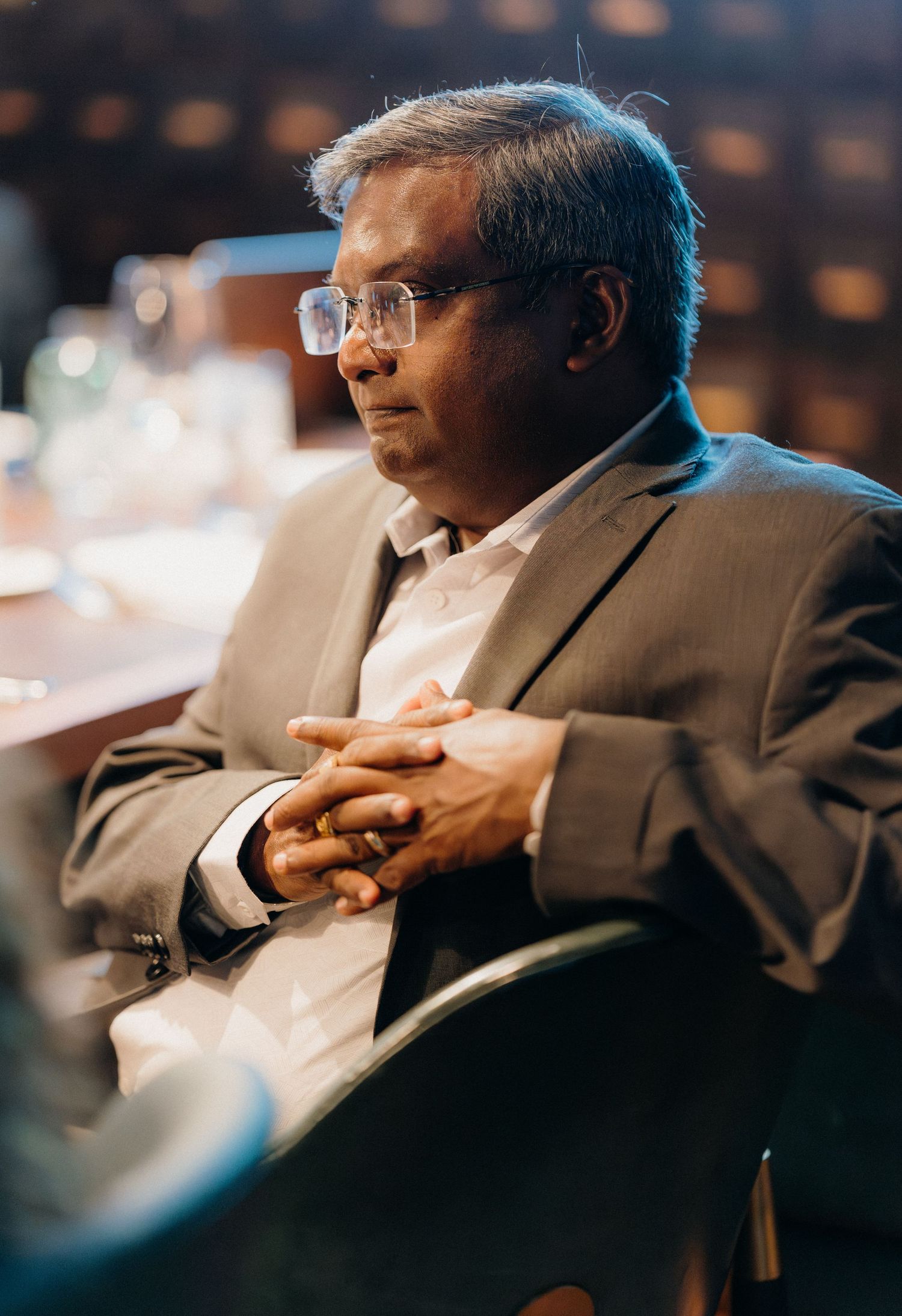 A person in a suit sits in contemplation during what appears to be a professional conference or meeting.