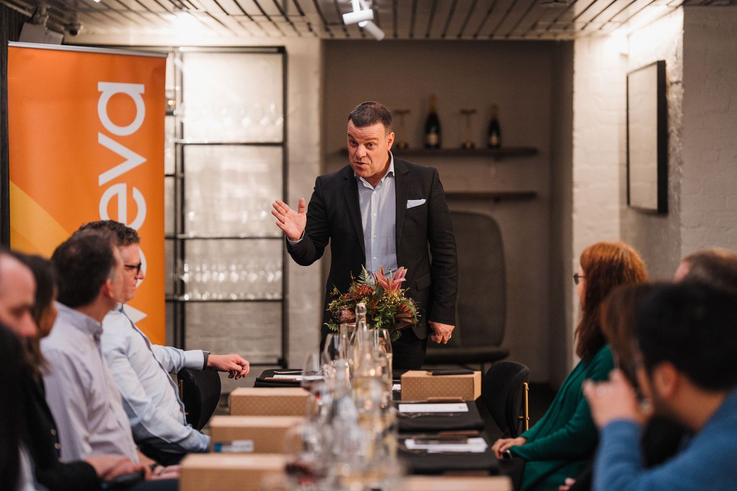 Business meeting in a modern conference room with orange accent walls and people gathered around a long table.